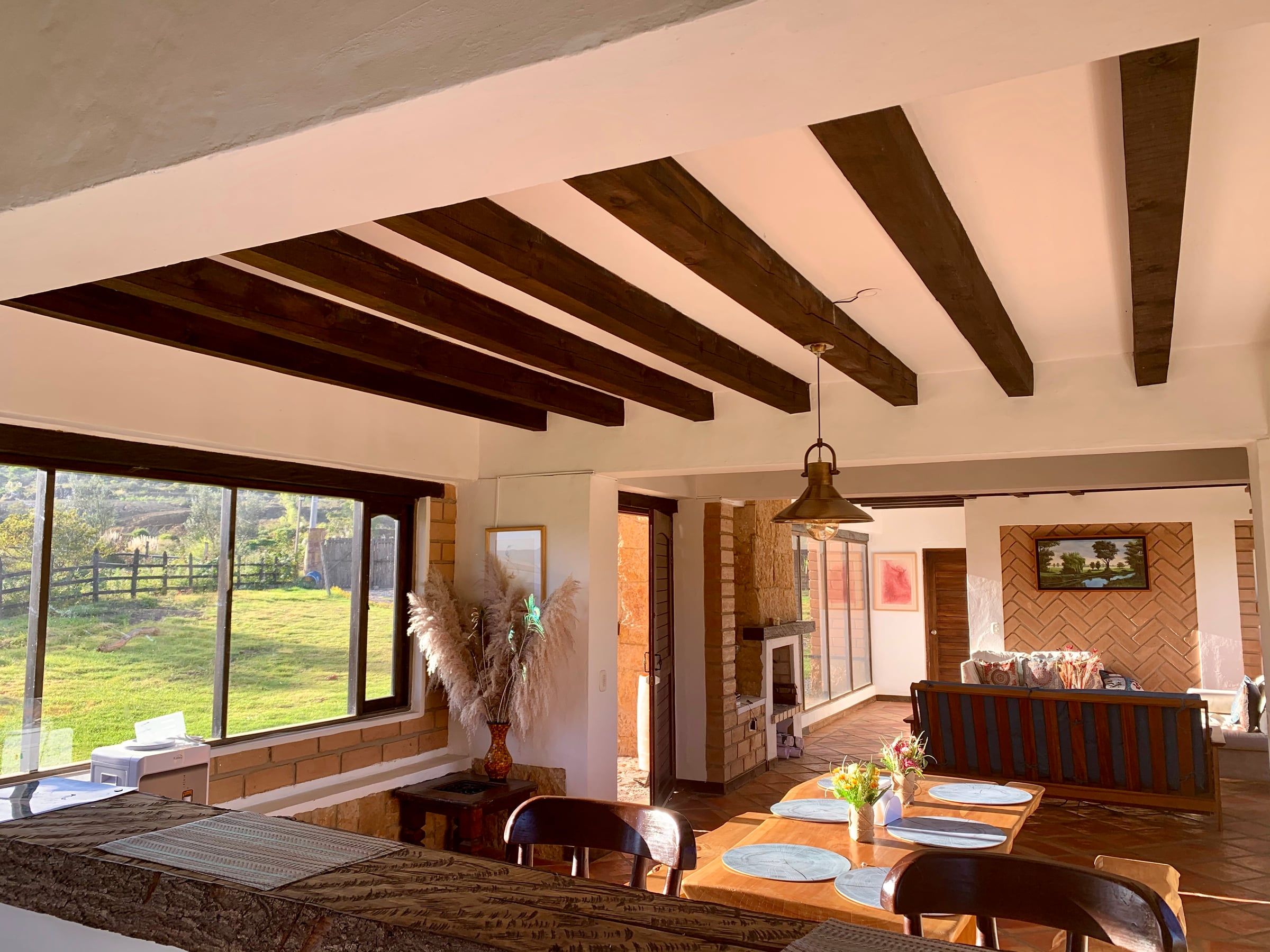 Sala y comedor integrados bajo vigas de madera, con ventanales hacia el prado