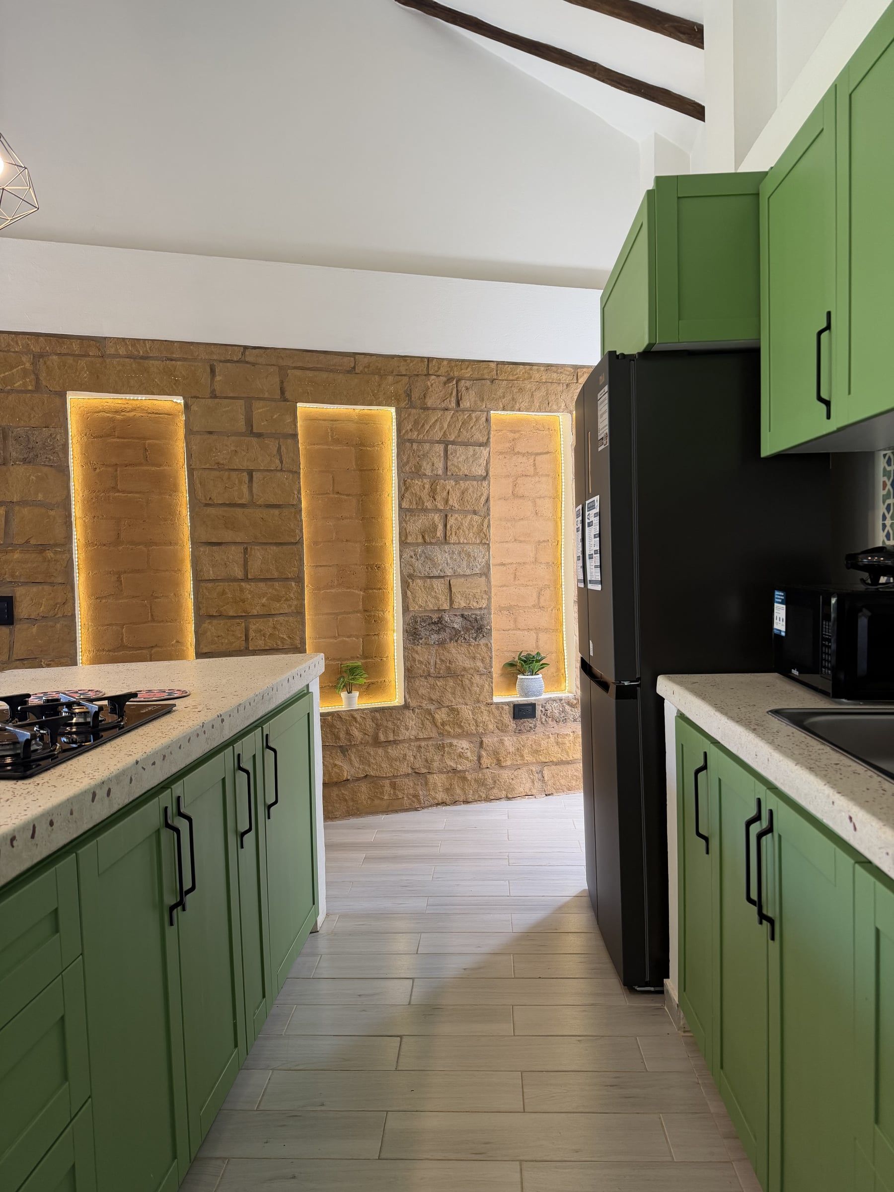 Cocina con muebles verdes y muro de piedra con nichos iluminados