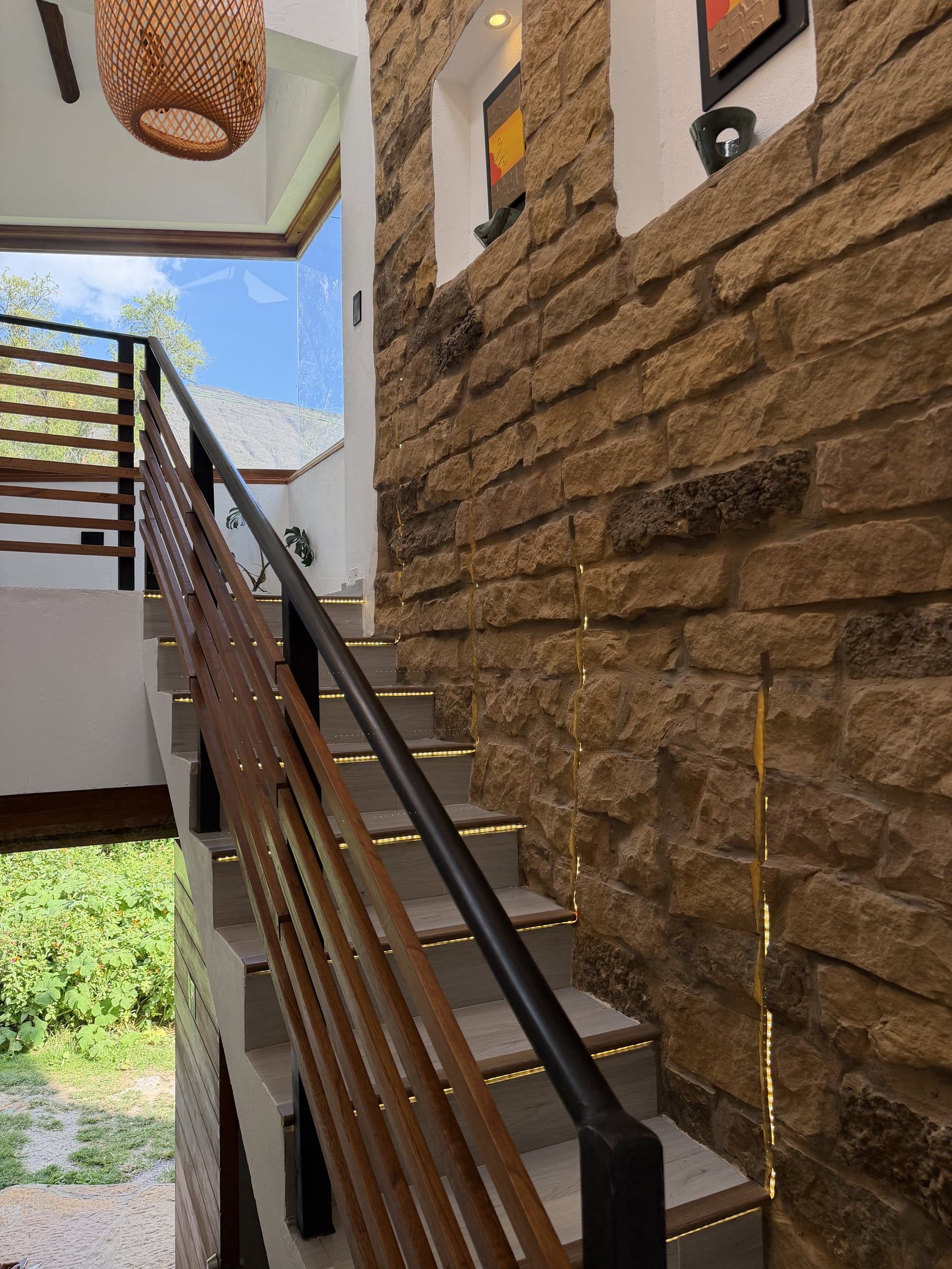 Escalera junto a un muro de piedra, con baranda metálica y luz natural desde lo alto