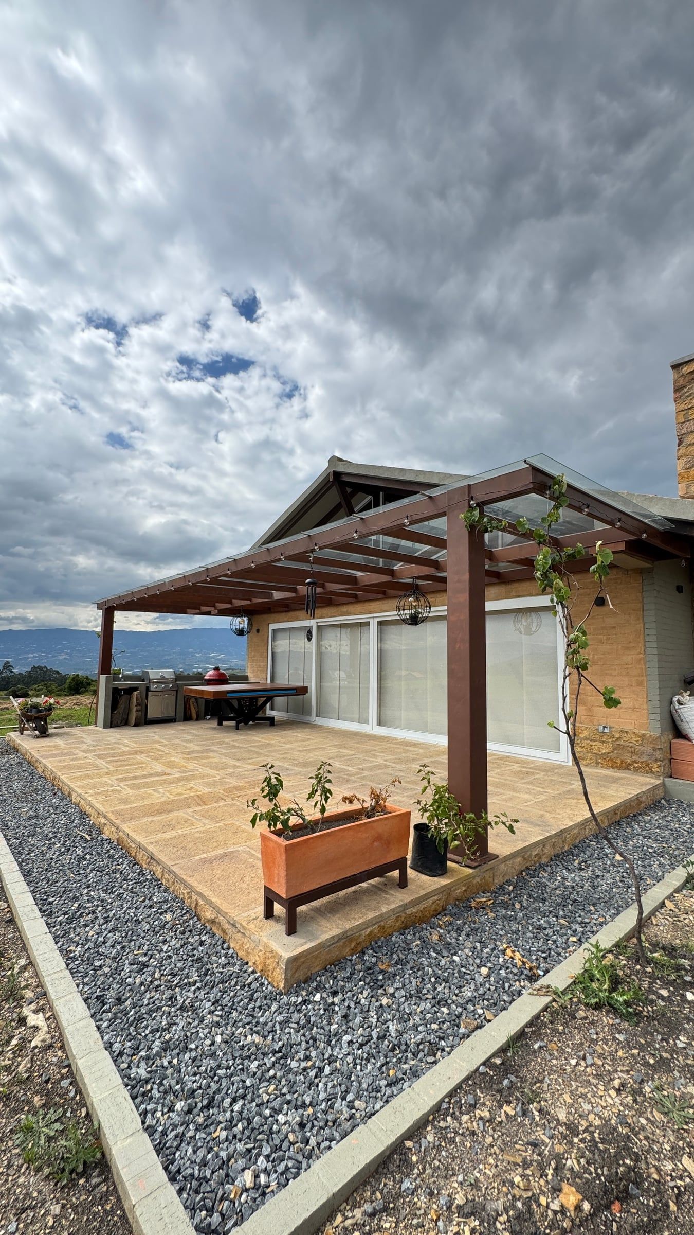 Terraza exterior con pérgola de madera y jardineras frente a la casa