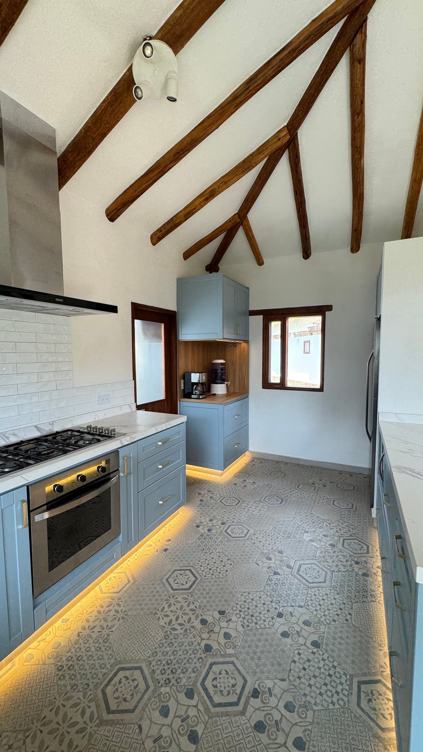 Casa Nido Verde después de la remodelación: otra vista de la cocina con estufa empotrada, horno, campana de acero y enchape blanco tipo metro