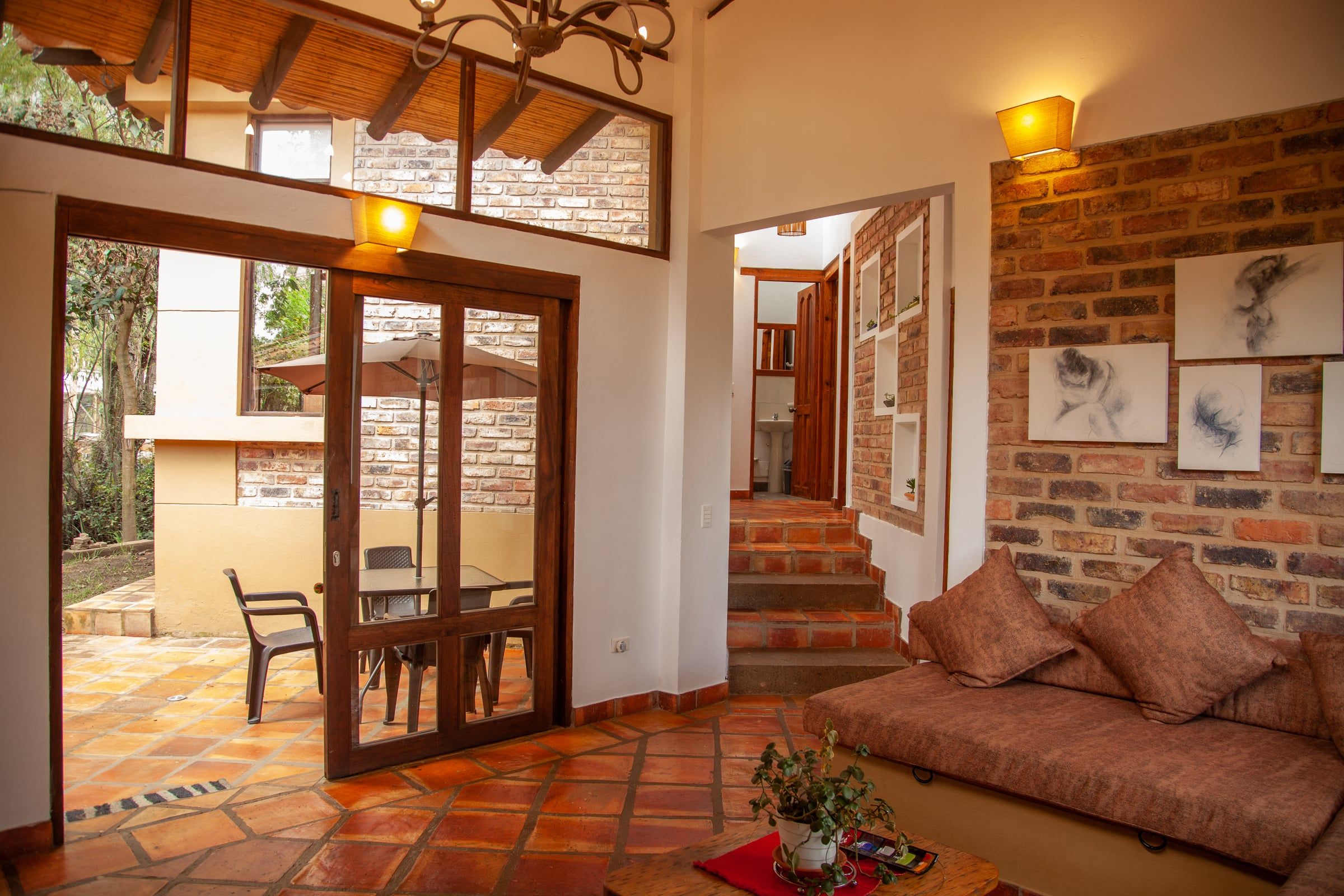 Sala de Clavellino House con muro de ladrillo a la vista, piso de baldosa de barro y puertas de madera hacia el patio