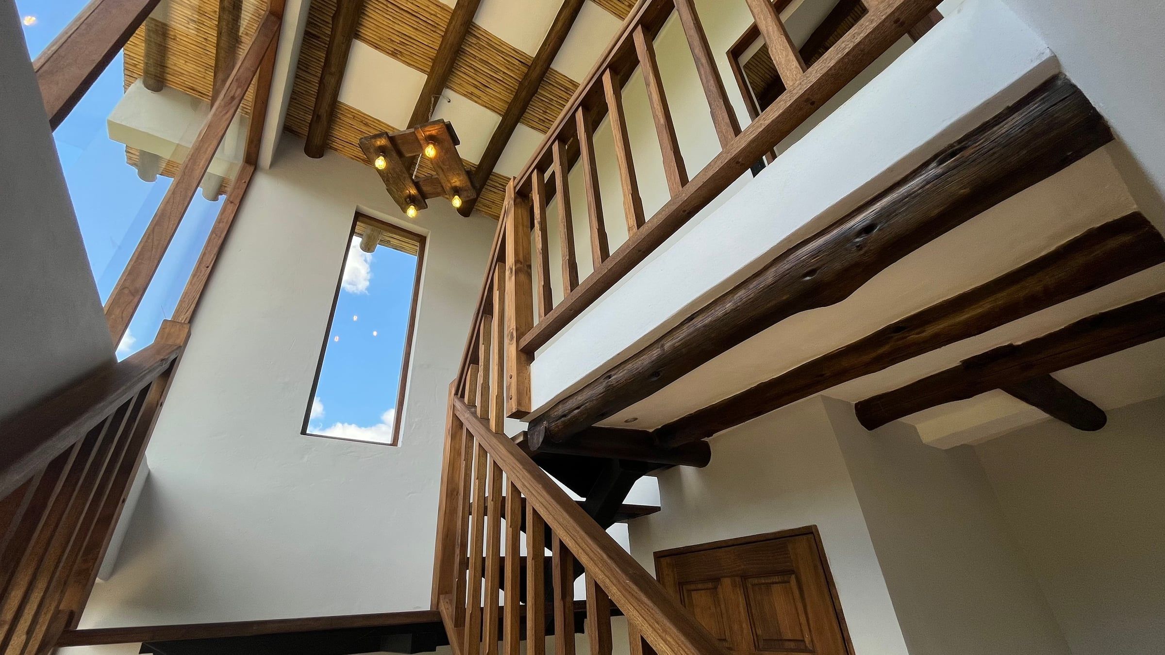 Escalera y baranda de madera hacia el segundo piso, iluminada por una ventana vertical
