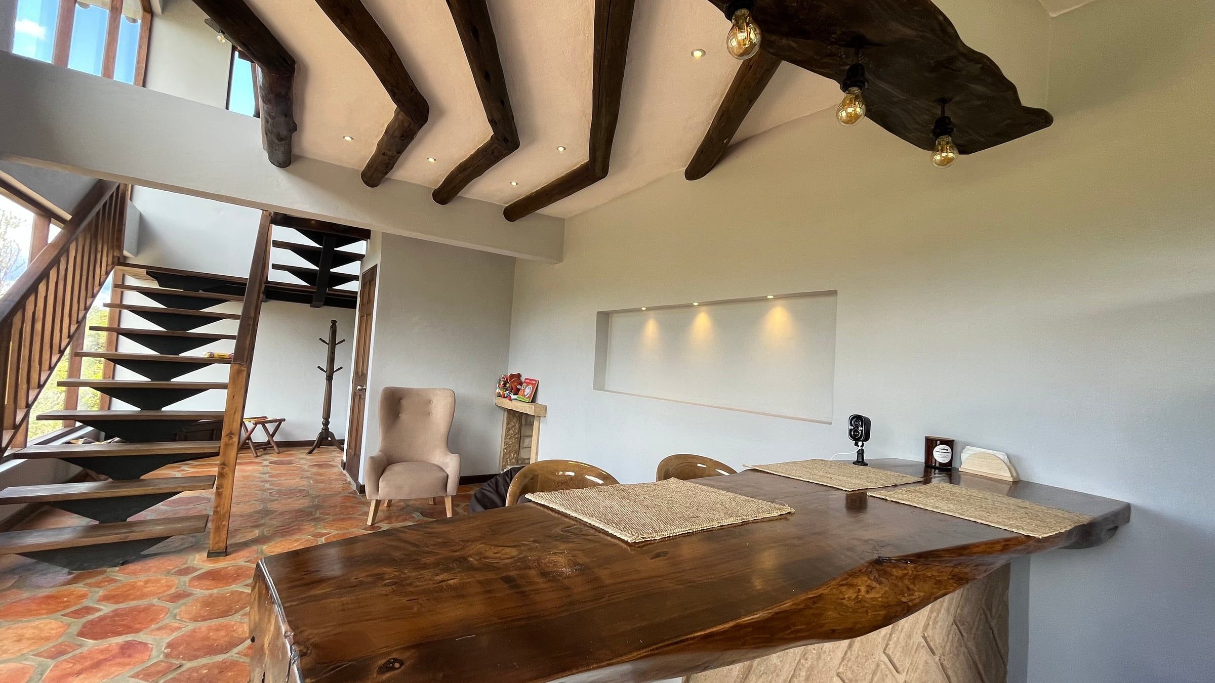 Zona social con mesa de madera, escalera y vigas de madera a la vista